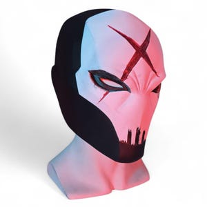 May include: A full-head mask featuring a white face with a prominent red X symbol on the forehead, black eye cutouts, and a black chin area. The sides and back of the mask are solid black, and the entire piece is displayed on a neck-shaped stand.