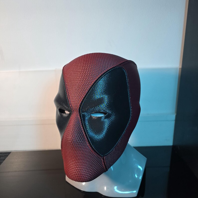 Puede incluir: Una m&aacute;scara de Deadpool roja y negra con una superficie texturizada. La m&aacute;scara tiene un &aacute;rea de ojos negra con una forma de ojo blanca.