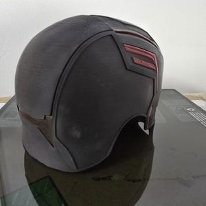 May include: A black helmet with red accents. The helmet has a smooth, rounded surface and a slightly pointed top. The red accents are in the shape of a stylised letter "F".