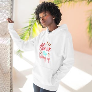 May include: A white hoodie with a front pocket and a drawstring hood. The hoodie features the text "Never Stop Looking Up" in red and teal script. The image shows a person wearing the hoodie.