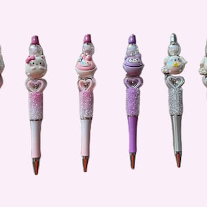 May include: Set of six sparkly pens with different character toppers. The toppers include a pink cat, a pink bird, a purple monster, a white bird, and two white birds with stars. The pens are pink, purple, and silver.