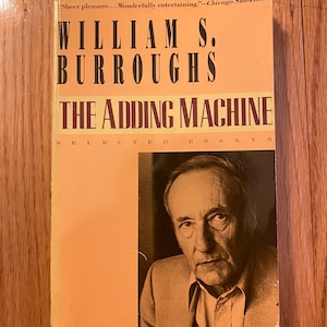 May include: A book cover with a yellow background and black text. The title is "The Adding Machine: Selected Essays" by William S. Burroughs. A black and white photo of the author is on the right side of the cover.