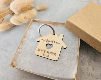 May include: A wooden house-shaped keychain with the text "our first home" and "BEN & MADDDY 2018". The keychain has a small heart cutout and is attached to a silver key ring.