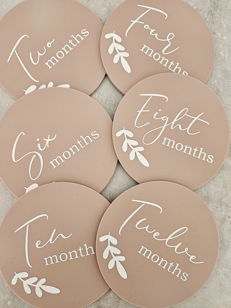 May include: Six round beige baby milestone cards with white text and leaves. The cards read "Two months", "Four months", "Six months", "Eight months", "Ten month", and "Twelve months".