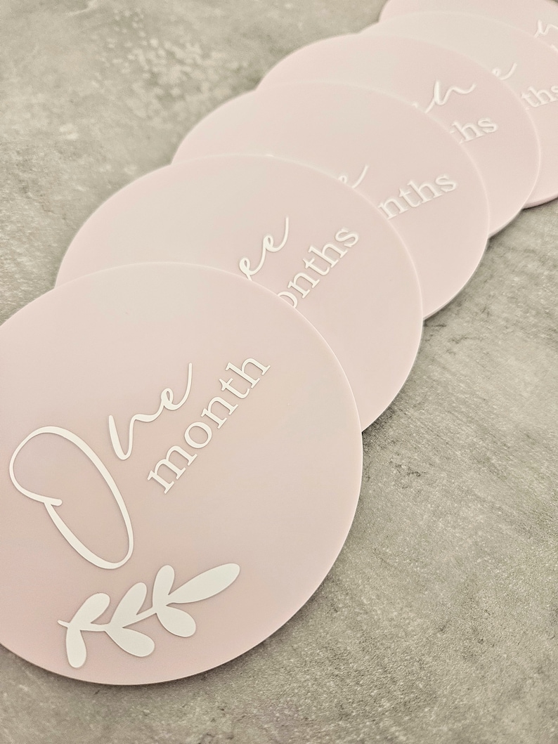 May include: A set of ten pink baby milestone cards with white text and a leafy design. The cards feature the phrases "One month", "Two months", "Three months", "Four months", "Five months", "Six months", "Seven months", "Eight months", "Nine months", and "Ten months".
