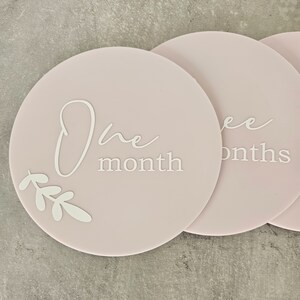 May include: A set of three pink baby milestone cards with white text and a leaf design. The cards read "One month", "Two months", and "Three months".