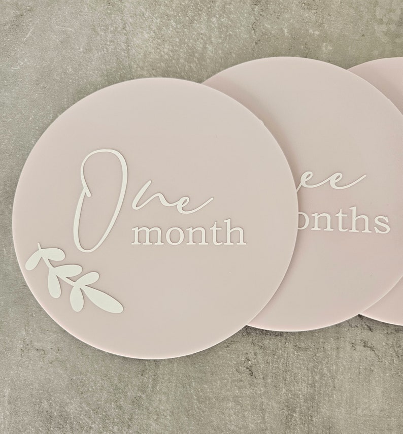 May include: A set of three pink baby milestone cards with white text and a leaf design. The cards read "One month", "Two months", and "Three months".