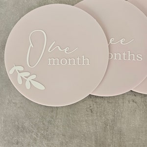 May include: Pink and white baby milestone photo prop discs with the text "One month" and "Three months".