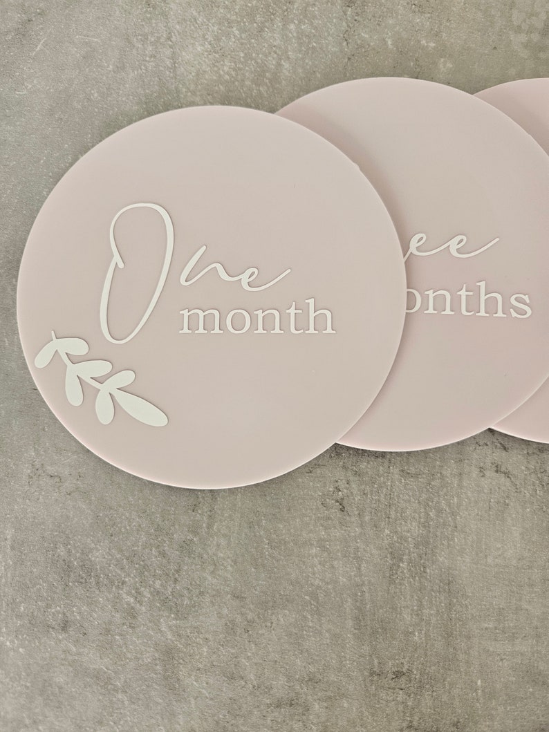 May include: Pink and white baby milestone photo prop discs with the text "One month" and "Three months".