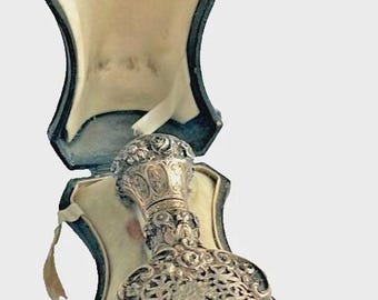 May include: A deep red glass scent bottle with a silver filigree overlay and a matching silver stopper, presented inside a dark blue, velvet-lined, hinged storage case with a cream-colored interior fabric and a secure metal clasp closure.