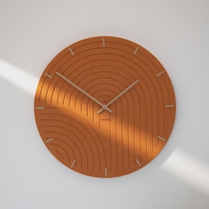 Può includere: Un orologio da parete rotondo arancione con un design strutturato unico. L'orologio presenta una serie di linee curve concentriche e lancette e indicatori di colore chiaro. L'orologio ha il testo "wonderfactory".