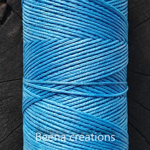 Puede incluir: Una bobina de cordón encerado azul brillante, ideal para manualidades y la elaboración de joyas. El cordón está enrollado apretado y tiene un acabado liso y pulido. El texto "Beena creations" está impreso en la bobina.