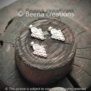 Pode incluir: Três pingentes de prata em forma de lágrima com um design de contas. Os pingentes estão sobre uma superfície de madeira castanho escura.