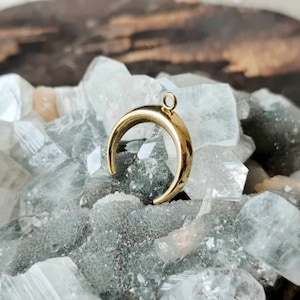 Peut inclure: Un pendentif en forme de croissant de lune en or avec une boucle en haut pour l'attacher à un collier ou un bracelet.
