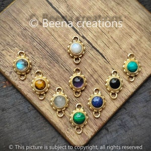 Peut inclure: Assortiment de 10 breloques connecteurs dorés avec des cabochons de pierres précieuses de différentes couleurs. Chaque breloque est dotée d'une double boucle pour la fixation aux bijoux.