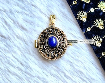 May include: A gold locket pendant with an ornate design and a blue gemstone in the center. The locket opens and closes with a hinge.