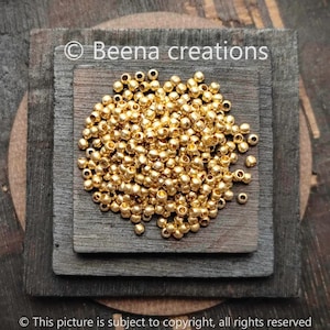 Peut inclure: Un tas de perles rondes de couleur dorée. Les perles sont petites et lisses, et elles sont disposées de manière aléatoire. Les perles sont sur une surface en bois.