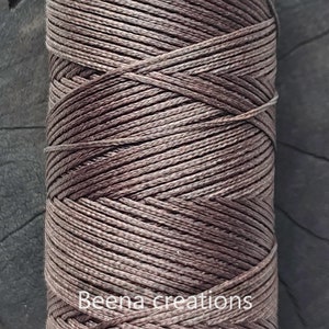 Könnte beinhalten: Nahaufnahme einer Spule mit braunem gewachstem Garn. Das Garn ist fest gewickelt und hat einen dezenten Glanz. Das Etikett auf der Spule lautet "Beena creations".