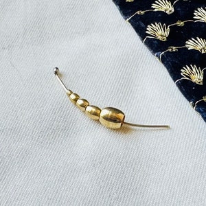 May include: A gold-toned metal bead chain with a small silver ball at the end. The chain is curved and has a total of six beads.