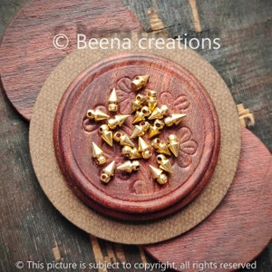 May include: A close-up of a small pile of gold-colored metal pyramid-shaped studs with a round base. The studs are on a wooden surface.