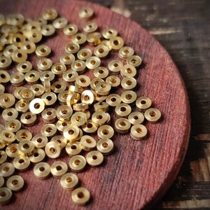 May include: A close-up of a pile of gold-coloured metal rings on a wooden surface. The rings are all the same size and shape, and they are arranged in a random pattern.