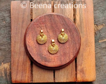 May include: Three gold-colored metal pendants with a circular design featuring concentric circles. The pendants are displayed on a wooden surface.