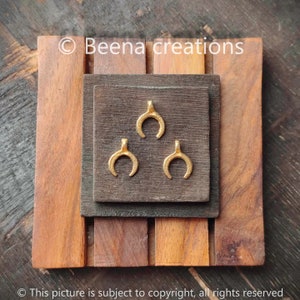 May include: Three gold-colored crescent moon shaped charms on a dark brown wooden surface.  © Beena creations