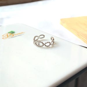 May include: A silver toe ring featuring a pattern of linked circles and small beads. The open design of the ring is visible, set against a white background. This elegant piece of jewellery is designed to be worn on the toe, adding a touch of sophistication.