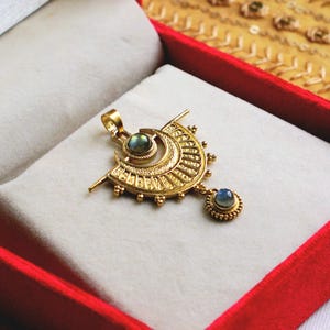 May include: A gold pendant featuring two blue gemstones. The pendant is shaped like a crescent moon with intricate detailing and a smaller pendant hanging from the bottom.