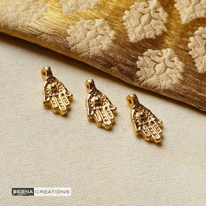Può includere: Tre ciondoli a forma di mano di hamsa dorati con un designo in rilievo. I ciondoli hanno un piccolo cerchio al centro del palmo.