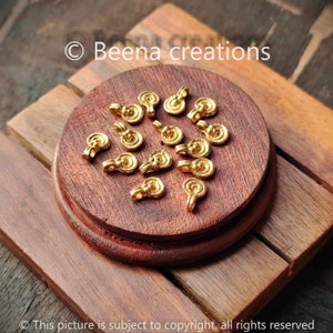 May include: A group of 15 gold-coloured metal charms with a swirl design. The charms are on a wooden surface.