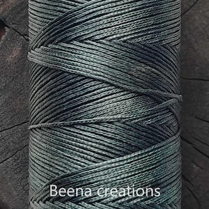 May include: A close-up of a spool of dark green and black embroidery floss. The floss is tightly wound and has a subtle sheen. The text "Beena creations" is visible at the bottom of the image.