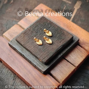 Puede incluir: Tres colgantes de hoja de oro con un pequeño bucle en la parte superior. Los colgantes están sobre una superficie de madera.