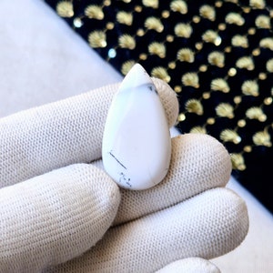 Puede incluir: Cabujón blanco en forma de lágrima con vetas negras. La piedra es lisa y pulida.