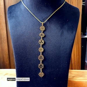 May include: A gold chain necklace featuring seven chakra symbols, each linked by a small chain. The necklace is displayed on a black velvet mannequin.