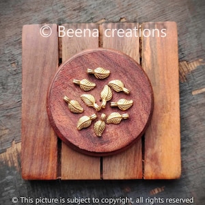 May include: A close-up of a wooden surface with a small round wooden plate. The plate is filled with 12 gold leaf-shaped metal charms.