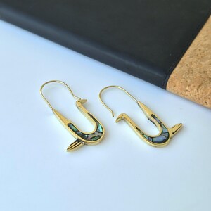 May include: A pair of gold-toned metal earrings shaped like stylized birds with long, curved ear wires. Each earring features an inlay of iridescent, multi-colored abalone shell along the body, creating a shimmering effect against the polished metal surface.