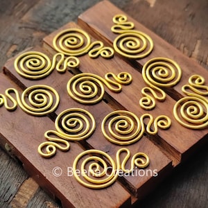 Könnte beinhalten: Zehn goldfarbene Metalldrahtspiralen, jede mit einer einzigartigen Form und einem einzigartigen Design, auf einer Holzoberfläche angeordnet. Die Spiralen haben einen Durchmesser von etwa 2,5 cm.