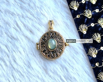 May include: A gold-toned locket pendant with an ornate design and a light green gemstone in the center. The locket is open and has a hinge on the side.