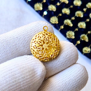 May include: A gold-colored pendant with a delicate, intricate design. The pendant is round and features a circular pattern of small, interconnected loops.