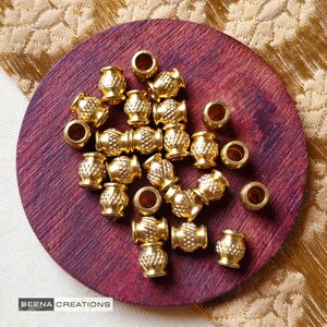 May include: A close-up of a pile of gold-colored metal beads with a textured surface. The beads are arranged on a dark red wooden surface.