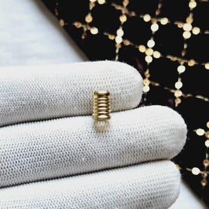 May include: A gold-colored metal ring with a ridged design. The ring is sitting on a white surface.