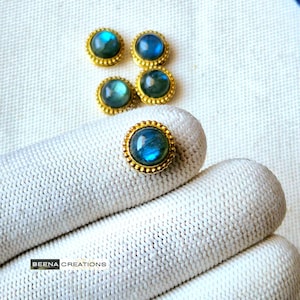 Può includere: Cinque montature rotonde dorate con pietre preziose di labradorite blu. Le montature hanno un bordo perlato.