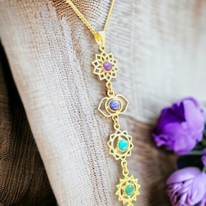 Puede incluir: Collar de cadena dorada con un colgante que representa los siete chakras, cada uno con una piedra preciosa de color diferente. Los chakras están dispuestos verticalmente, comenzando por el chakra corona en la parte superior y terminando con el chakra raíz en la parte inferior.