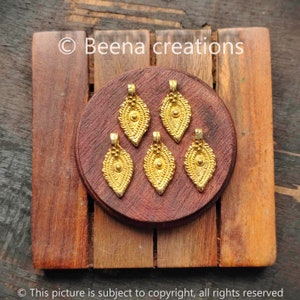 Puede incluir: Cinco colgantes de hoja de oro con diseños intrincados. Cada colgante tiene un pequeño círculo en el centro y está rodeado por un borde detallado.