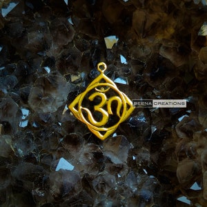 May include: Gold-colored Om symbol pendant with a third eye design, set against a background of dark brown crystals.