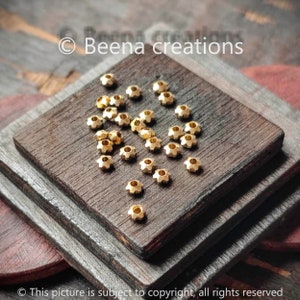 Pode incluir: Um close-up de um grupo de contas de metal douradas com um design em forma de estrela. As contas estão espalhadas sobre uma superfície de madeira.