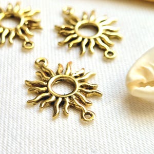 May include: Three gold-toned sun charm pendants with a circle in the centre and rays extending outwards. Each charm has two jump rings for attaching to jewellery.