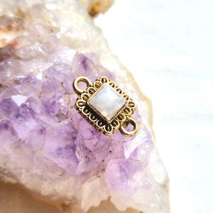 Puede incluir: Conector dorado con una piedra de luna cuadrada. El conector tiene dos bucles para sujetar piezas de joyería.