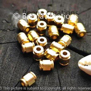 May include: A close-up of a group of gold-colored metal connectors. The connectors are small and round, with a hole in the center. They are arranged in a random pattern on a dark wooden surface.